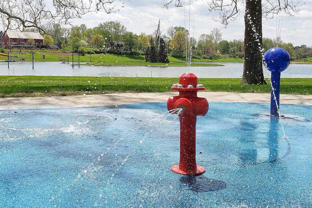 Red fire hydrant water play feature spraying water at a dog water park beside a blue ball feature