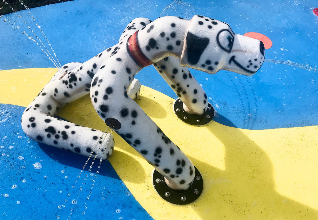 Close-up of a sitting dog water play feature spraying water at a colorful dog water park